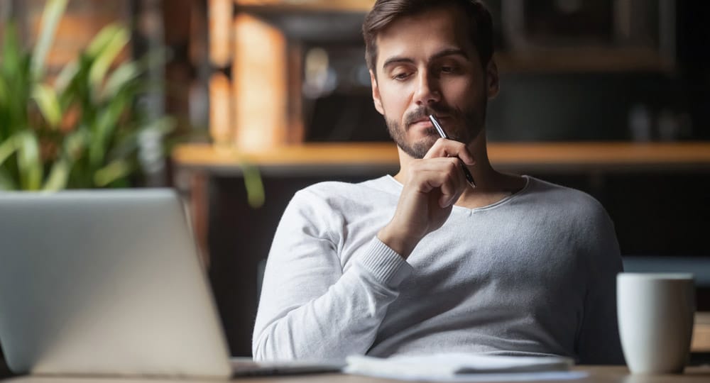 Man collecting thoughts to write down while sitting in front of a laptop
