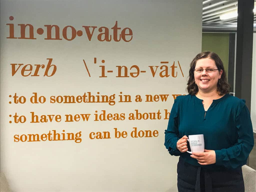 Woman standing in front of wall that defines "innovate"